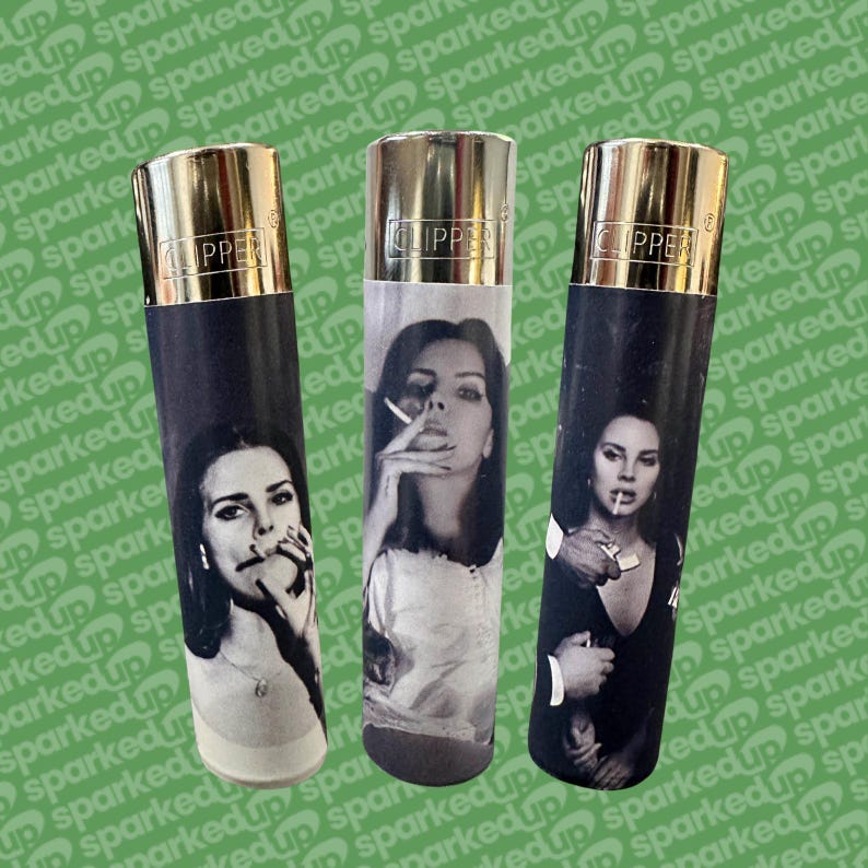 May include: Three Clipper lighters with gold tops and black and white images of a woman smoking. The lighters have a cylindrical shape and are displayed against a green background with the word "sparked up" repeated.