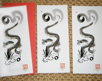 May include: Three rectangular white cards featuring a black ink wash painting of a dragon with a long, swirling body. Each card includes a small red square seal at the top left and a larger red square stamp with text at the bottom right.