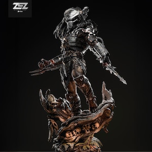 May include: A detailed statue of a Predator warrior, standing on a base adorned with skulls and organic textures. The figure is clad in dark armor, holding bladed weapons, and features a masked face. The statue is a collectible item.