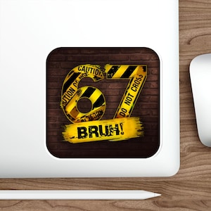May include: A sticker with a brick background features a yellow and black caution sign design. The number "67" is prominently displayed, along with the words "CAUTION" and "DO NOT CROSS". The word "BRUH!" is written in a yellow brushstroke.