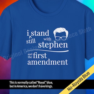May include: Royal blue t-shirt with white text: "i stand still with stephen and the first amendment." A graphic of a person with glasses is above the word "stephen." The shirt has a "No-Royals Blue" tag.