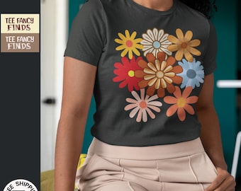 May include: A black t-shirt with a colorful floral design. The flowers are in shades of red, orange, yellow, blue, and pink. The shirt has a crew neck and short sleeves. "TEE FANCY FINDS" is printed on the shirt.