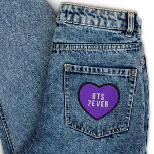 May include: A pair of blue denim jeans with a purple heart-shaped patch that says "BTS 7EVER" on the back pocket.