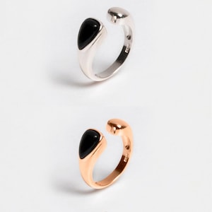 Peut inclure: Deux bagues ouvertes, une argentée et une en or rose, chacune ornée d'une pierre noire en forme de goutte. Les bagues sont présentées sur fond blanc. Le nom de la marque "ÉCLAT" est en bas.