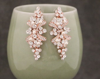 May include: Rose gold dangle earrings with a cascading design of clear rhinestones and white pearls.