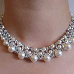 May include: A silver and white pearl necklace with a geometric design. The necklace features large, round pearls and smaller, sparkling rhinestones.