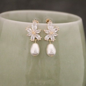 May include: A pair of gold earrings with a flower design and a pearl drop. The earrings are made of gold and have a clear crystal flower design with a pearl drop.