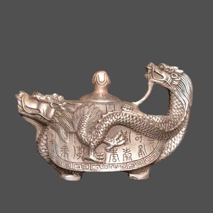 Könnte beinhalten: Eine silberne Teekanne in Form einer Schildkröte mit einem Drachenhenkel. Die Teekanne ist mit chinesischen Schriftzeichen und filigranen Details verziert.