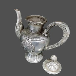 May include: A silver teapot with intricate floral designs and a matching lid. The teapot has a spout shaped like a bird's head and a handle with a decorative design.