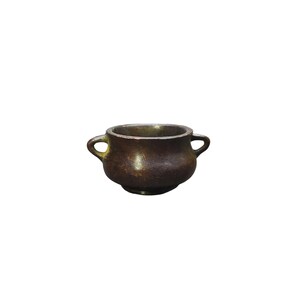 May include: A small, antique-style bronze bowl with two loop handles. The bowl has a rounded body and a dark, aged patina, suggesting it is made of metal. The design is simple and functional, suitable for decorative or practical use.