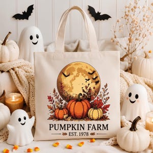 Peut inclure: Un sac fourre-tout en toile couleur crème avec une illustration représentant une grande pleine lune, des chauves-souris en vol et trois citrouilles entourées de feuillage d'automne. Le texte PUMPKIN FARM EST. 1978 est imprimé en noir.