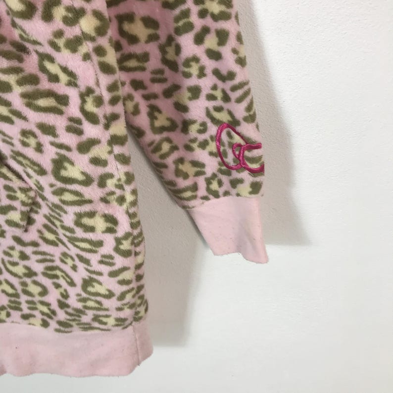 Puede incluir: Sudadera con capucha de forro polar rosa y verde oliva con estampado de leopardo. La sudadera con capucha tiene pu&ntilde;os y dobladillo rosas. Un logotipo rosa bordado est&aacute; en la manga. La tela tiene una textura suave y afelpada.