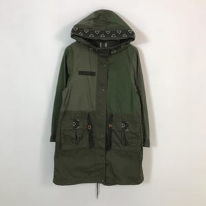 Könnte beinhalten: Eine lange, olivgrüne Kapuzenjacke mit einem geometrischen Muster am Kapuzenrand. Die Jacke hat ein farbblockiertes Design mit zwei Grüntönen, zwei Vordertaschen und einem Kordelzug in der Taille. Die Jacke ist zugeknöpft.