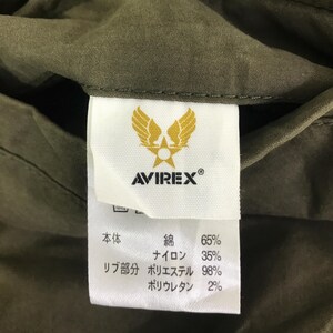 May include: A white fabric clothing tag sewn into an olive green garment. The tag features a yellow winged star logo above the text AVIREX. Below, Japanese text lists material composition as 65% cotton, 35% nylon, 98% polyester, and 2% polyurethane.