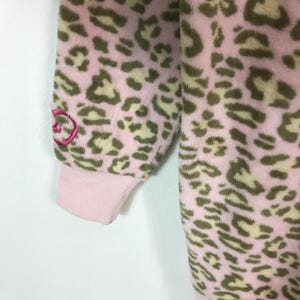 Puede incluir: Manga de pijama de forro polar rosa y marr&oacute;n con estampado de leopardo y pu&ntilde;o rosa. La manga tiene un peque&ntilde;o dise&ntilde;o bordado en rosa en la parte superior del brazo. La tela del pijama es suave y afelpada.
