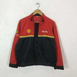 May include: Red, black, and yellow racing jacket with the Shell and Helix logos. The jacket has a stand-up collar, a zipper closure, and a Ferrari logo on the left sleeve. The jacket is made of a lightweight material.