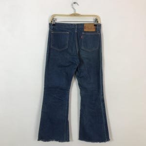 May include: Dark blue denim jeans with a flared leg design, featuring two back pockets and a leather patch with the brand name "EDWIN". The jeans are hanging on a metal hanger.