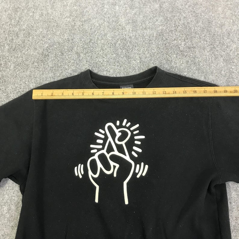 K&ouml;nnte beinhalten: Schwarzes Sweatshirt mit Rundhalsausschnitt und wei&szlig;er Grafik einer Hand, die ein gekreuztes Fingerzeichen macht. Das Sweatshirt wird mit einem Lineal gemessen, was eine L&auml;nge von ca. 48 cm zeigt.