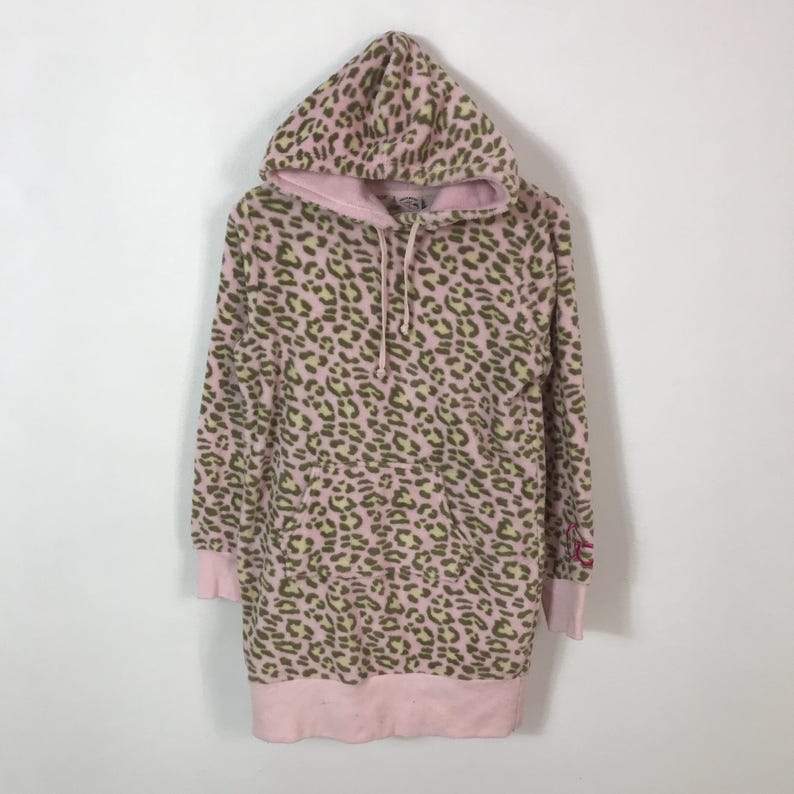 Puede incluir: Vestido sudadera con capucha rosa con estampado de leopardo en tonos marr&oacute;n y amarillo. El vestido tiene capucha con cord&oacute;n, mangas largas y dobladillo y pu&ntilde;os de canal&eacute; rosas. Un peque&ntilde;o logo es visible en la manga.