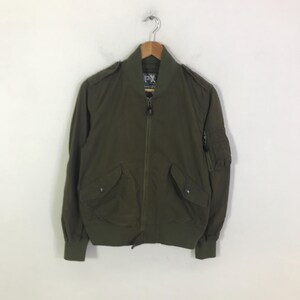May include: An olive green bomber jacket featuring a full-length front zipper, a ribbed collar, cuffs, and hem. The jacket includes two front flap pockets with snap closures, shoulder epaulets, and a zippered utility pocket on the left sleeve.