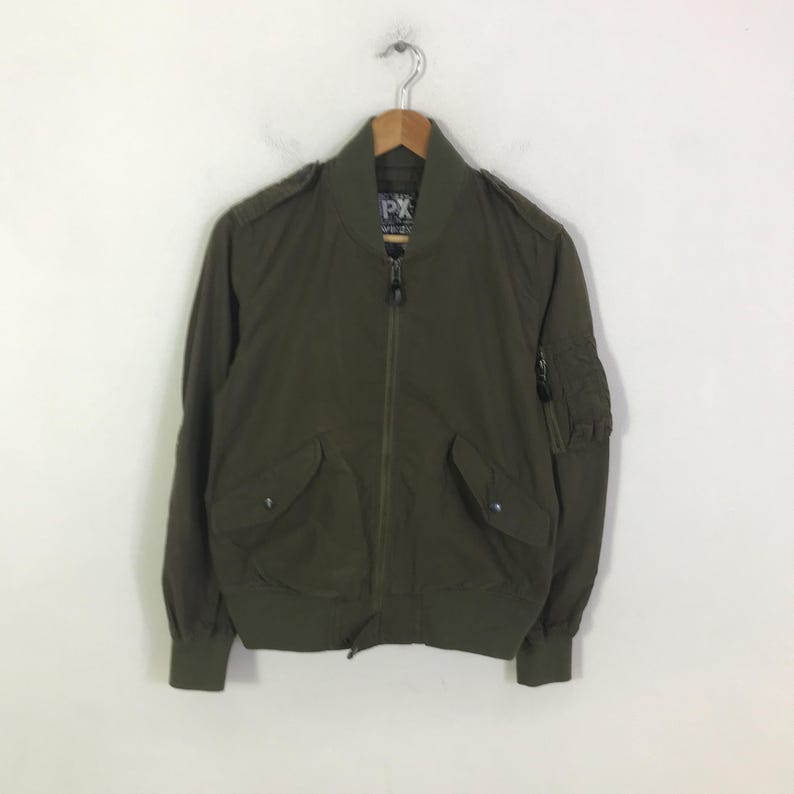 May include: An olive green bomber jacket featuring a full-length front zipper, a ribbed collar, cuffs, and hem. The jacket includes two front flap pockets with snap closures, shoulder epaulets, and a zippered utility pocket on the left sleeve.