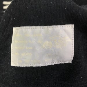 K&ouml;nnte beinhalten: Nahaufnahme eines schwarzen Kleidungsst&uuml;cks mit einem wei&szlig;en Etikett. Das Etikett hat Text und eine Grafik eines Motorrads. Der Text ist hellgelb.