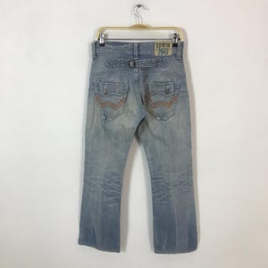 May include: Light blue denim jeans with distressed details, featuring a back belt loop and pockets with orange stitching. The jeans have a faded wash and the "EDWIN 40" logo patch.
