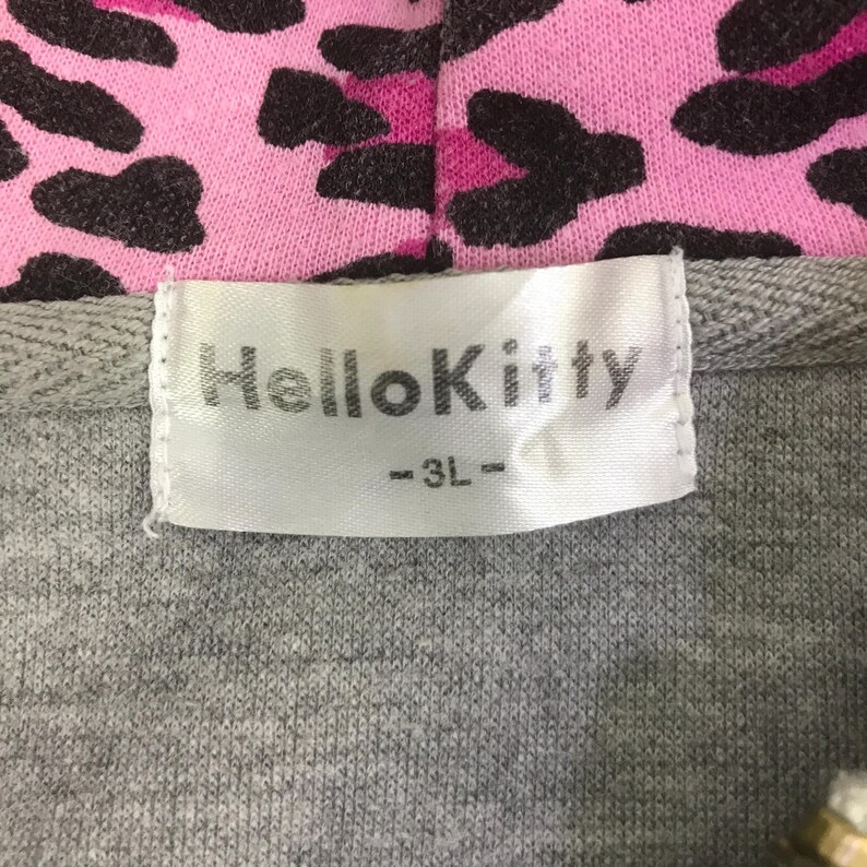 May include: Close-up of a gray hoodie with a pink and black leopard print hood lining. The label reads "Hello Kitty" in white text.