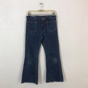 May include: Dark blue denim jeans with a flared leg design. The jeans have two front pockets and two back pockets. The hem of the jeans is frayed. The jeans are hanging on a metal hanger.