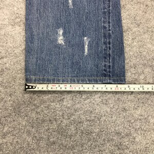 May include: Close-up of blue denim jeans with distressed details. A measuring tape shows the jeans are approximately 10 inches wide. The jeans are on a gray surface.