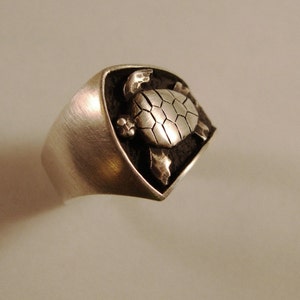 May include: A silver ring with a detailed turtle design. The turtle is raised and has a textured shell.