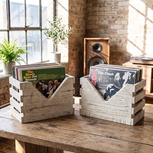 May include: Two rectangular white wooden crates with a V-shaped cutout on the front panel, each filled with vinyl records. The crates feature a distressed finish, showing wood grain texture. One crate holds The Beach Boys Pet Sounds album.