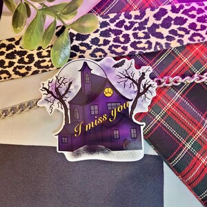 May include: A purple and black haunted house sticker with a full moon and two bare trees. The text "I miss you" is written in yellow on the sticker.