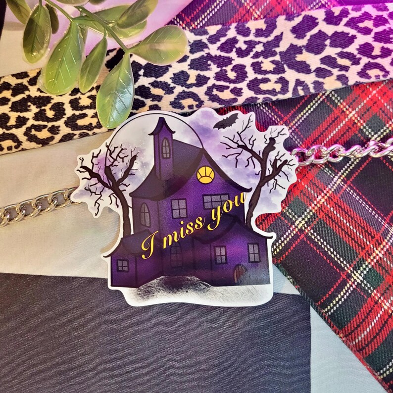 May include: A purple and black haunted house sticker with a full moon and two bare trees. The text "I miss you" is written in yellow on the sticker.