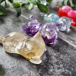 May include: Five small resin animal figurines in various colors. The figurines are shaped like cats and are made of clear resin with embedded glitter and other decorative elements.