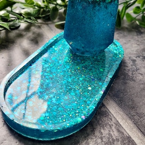 May include: A turquoise blue ring dish with a matching turquoise blue ring holder. The dish and holder are made of resin and have a glittery finish.