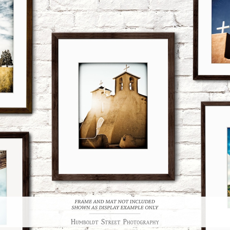 May include: A sepia-toned photograph of a church with two bell towers and a cross on top of each tower. The church is made of adobe brick and has a rustic, weathered look. The sun is shining brightly in the background, creating a warm glow.
