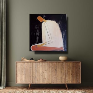 May include: Abstract painting of a figure in a kneeling position. The figure is depicted with a white body, orange head and legs, and black background. The artwork is displayed on a wooden cabinet.