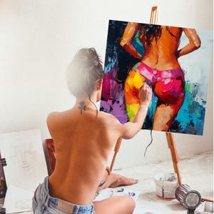 May include: A person paints a colorful abstract painting of a woman wearing a pink bikini bottom. The painting is on an easel and the person is sitting on the floor with their back to the viewer.