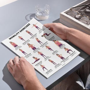 May include: A person holding a white printed sheet titled "MOBILITY EXERCISES". The sheet displays various exercise illustrations with text labels. The exercises include arm circles, leg swings, and hip openers. A glass of water and a box with glasses are in the background.