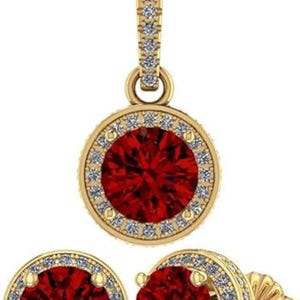 May include: A gold-toned jewelry set featuring a pendant necklace and matching stud earrings. Each piece has a large, round, deep red gemstone surrounded by a halo of smaller, clear stones. The pendant hangs from a delicate chain.