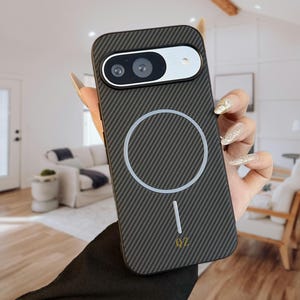 Può includere: Una custodia per telefono grigio scuro con una trama in fibra di carbonio. La custodia presenta un ritaglio per la fotocamera, un design circolare bianco e le lettere "QZ" in basso. La custodia è tenuta da una persona con unghie lunghe.