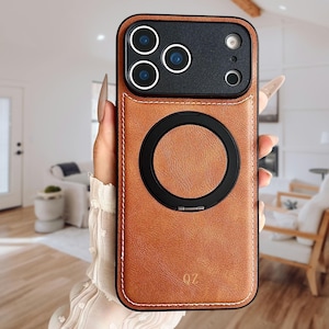 Puede incluir: Una funda de teléfono de cuero marrón con un módulo de cámara negro y un anillo magnético circular negro. La funda tiene costuras blancas alrededor de los bordes y las letras "OZ" son visibles en la esquina inferior derecha.