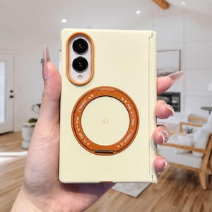 May include: A pale yellow foldable phone case featuring a prominent orange circular ring stand on the back. The case includes an orange camera lens bezel and text around the ring that reads 360 degree rotation free with star icons.