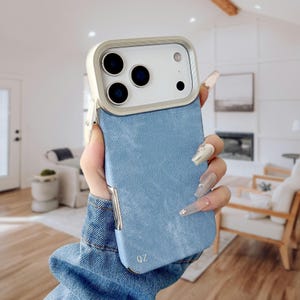 Pode incluir: Capa de telefone azul claro com textura de ganga e moldura e contorno da câmara prateados. A capa tem uma textura de ganga azul clara na parte traseira e nas laterais. As letras "QZ" estão impressas na parte inferior.