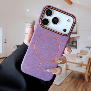 May include: A lilac phone case featuring an orange circle and trim. The case has a textured finish and a camera aperture with orange and black detailing. The letters "QZ" are printed on the lower left side of the case.