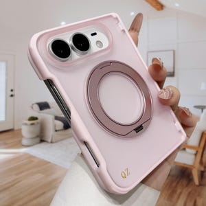 May include: A light pink smartphone case featuring a metallic rose gold circular ring stand on the back. The case has a raised camera cutout with two circular lenses visible and the letters QZ printed in gold near the bottom corner.
