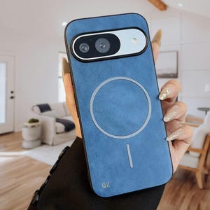 Può includere: Una custodia blu per telefono con un ritaglio per la fotocamera e un design circolare bianco. La custodia ha un aspetto strutturato e le lettere "QZ" sono visibili nell'angolo in basso. La custodia è tenuta da una persona.