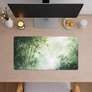 Desk mat with a green bamboo forest design, placed on a light wood desk with a computer, tablet, and blue hydrangea flowers in a gray pot.