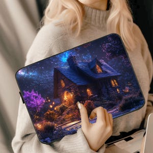 Op de afbeelding: Een laptophoes met een fantasierijk ontwerp met een stenen huisje met gloeiende ramen, omringd door weelderig groen onder een sterrenhemel.
